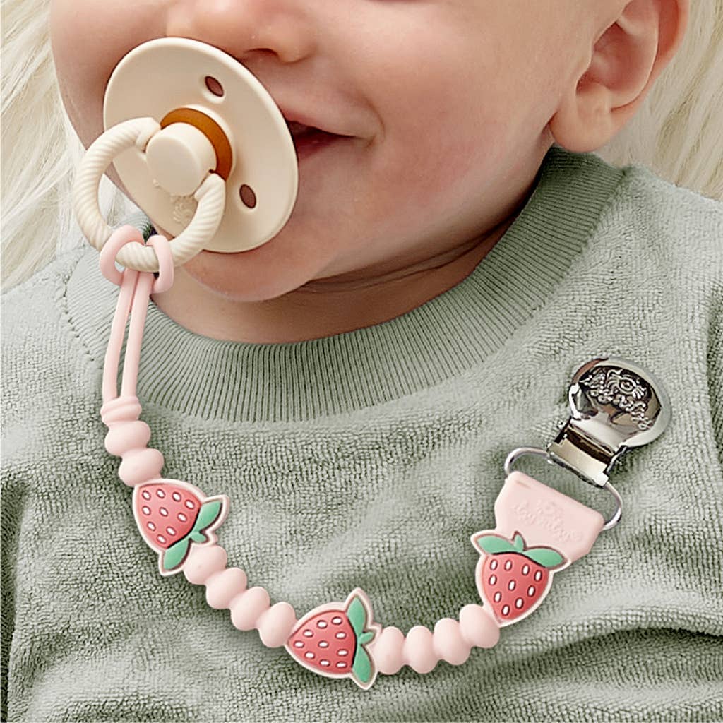 Baby wearing a pacifier with a strawberry-themed clip on a light green background