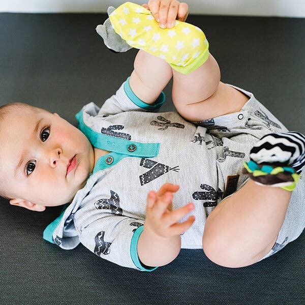 Baby lying on a dark surface holding  yellow socks with white polka dots.